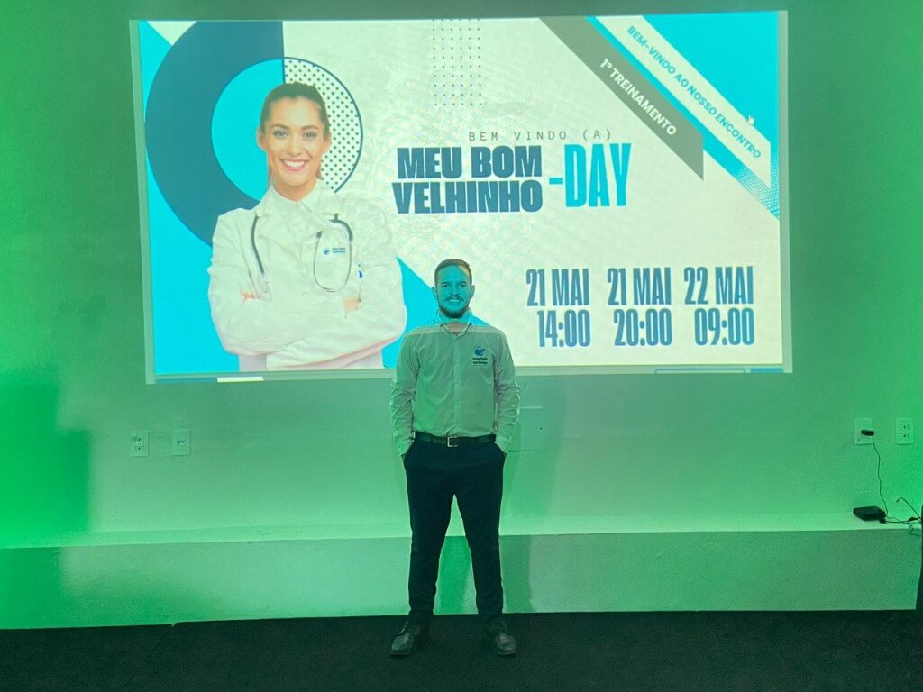 Renan Willian Costa durante a convenção interna Meu Bom Velhinho Day, cercado por materiais institucionais